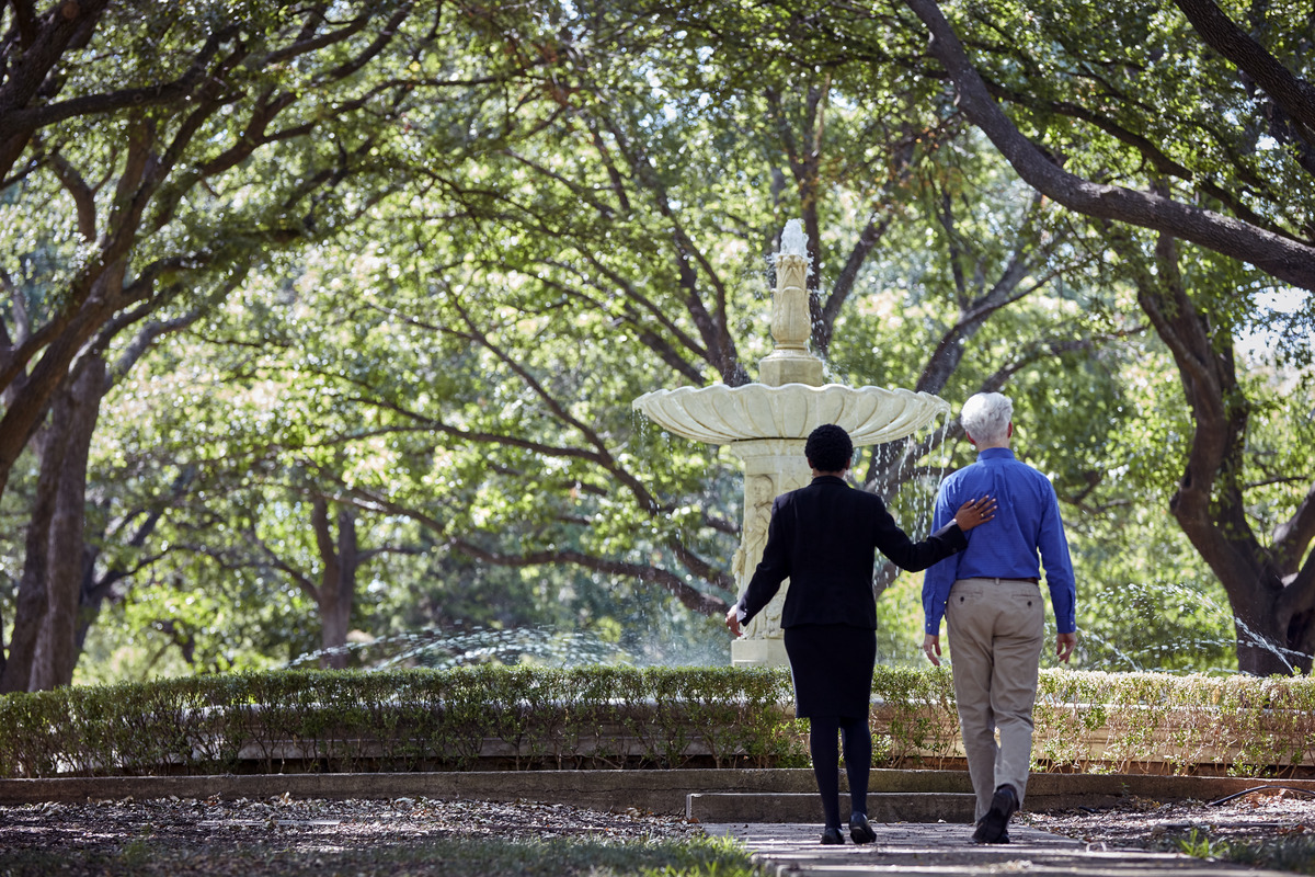 An associate walks a man near a fountain on cemetery grounds.