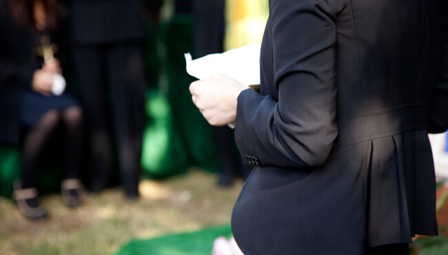 Mourner in a suit reads at a funeral service