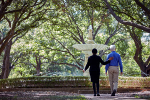 An associate walks a man near a fountain on cemetery grounds.